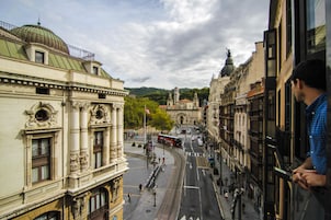 Vista da rua com edifícios históricos, um bonde e céu claro.