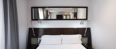 A hotel room with a large bed, two bedside tables, a nightstand, a mirror, and a desk with a lamp.