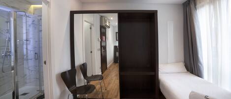 Habitación de hotel moderna con un espejo grande, suelo de madera, cama con edredón blanco y zona de ducha.