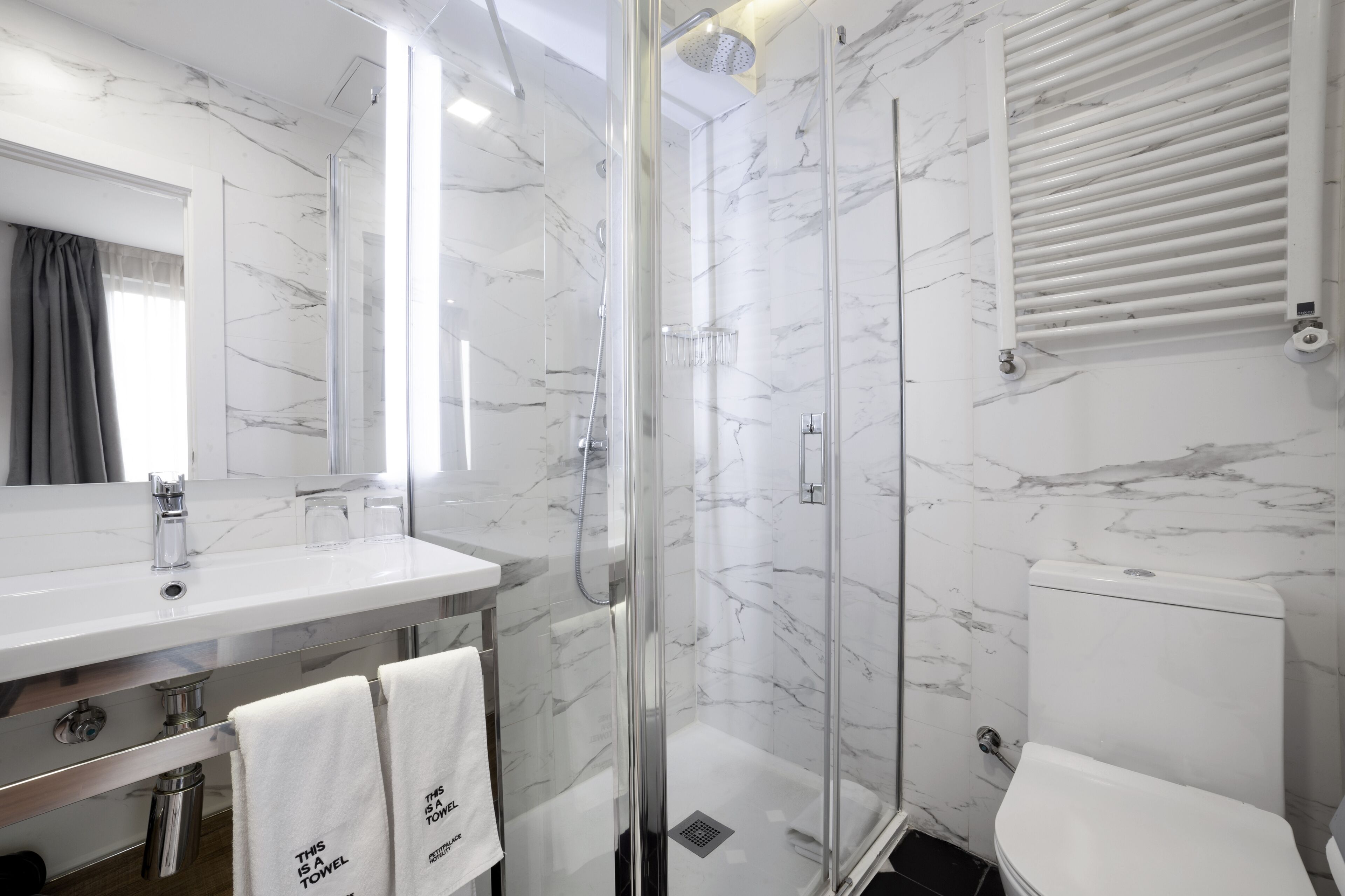 A modern bathroom with a glass-enclosed shower, a white marble sink, and a toilet.