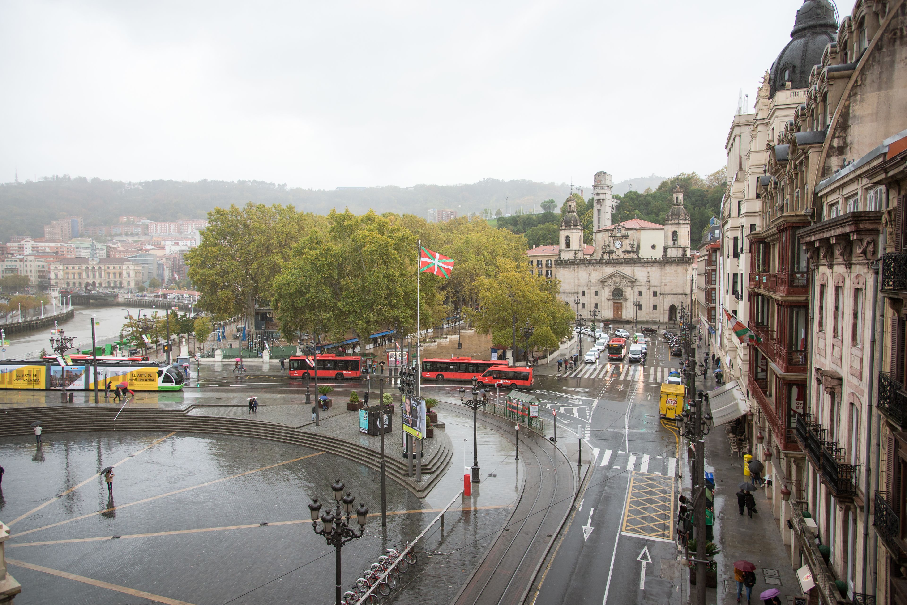 A city square with tram lines, a flag, and buildings.