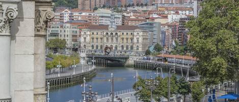 A riverside view of a city with historic buildings, a bridge, and a waterfront promenade.