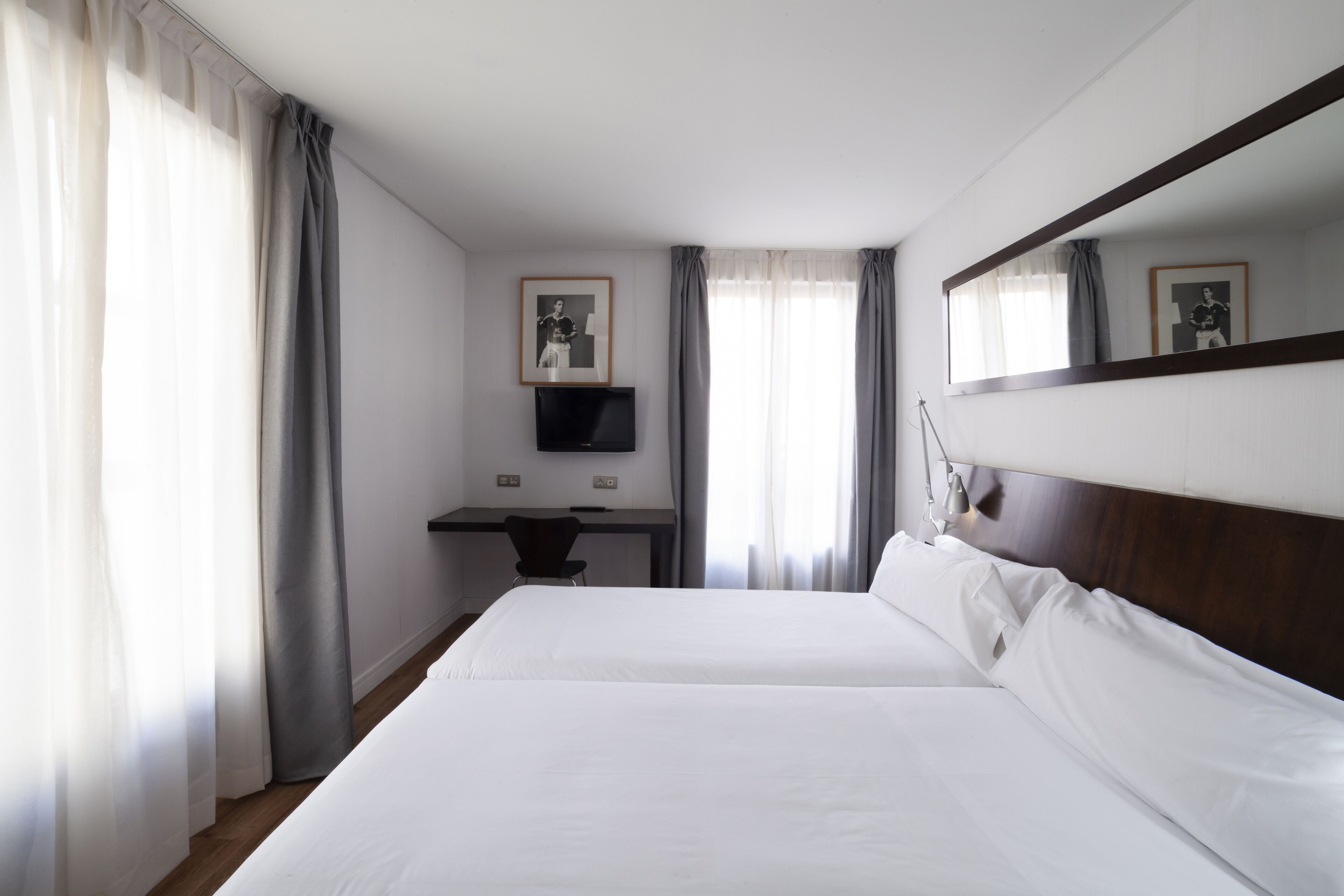 A hotel room with two beds, a desk, a TV, and a large mirror.