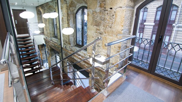 A staircase with wooden steps and metal railings, leading to a stone wall with arched windows. - Petit Palace Arana (Bilbao)