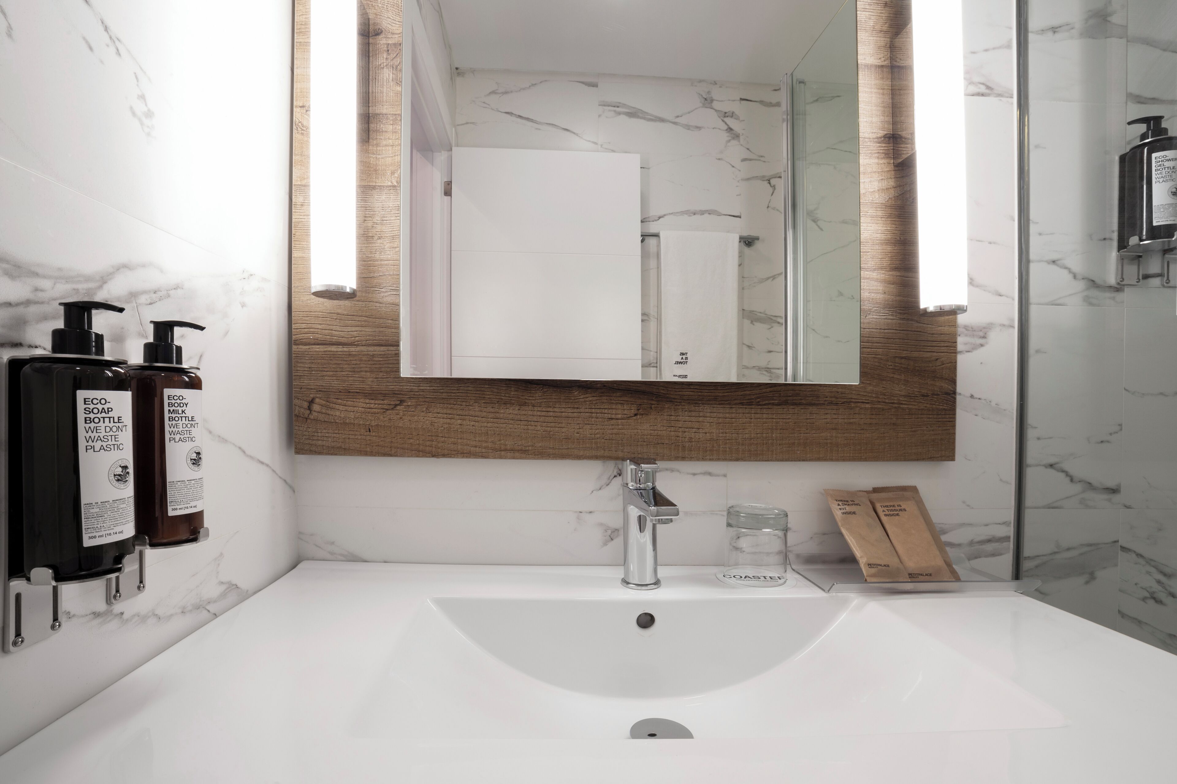 A bathroom with a white sink, a wooden-framed mirror, and two eco-friendly soap dispensers.