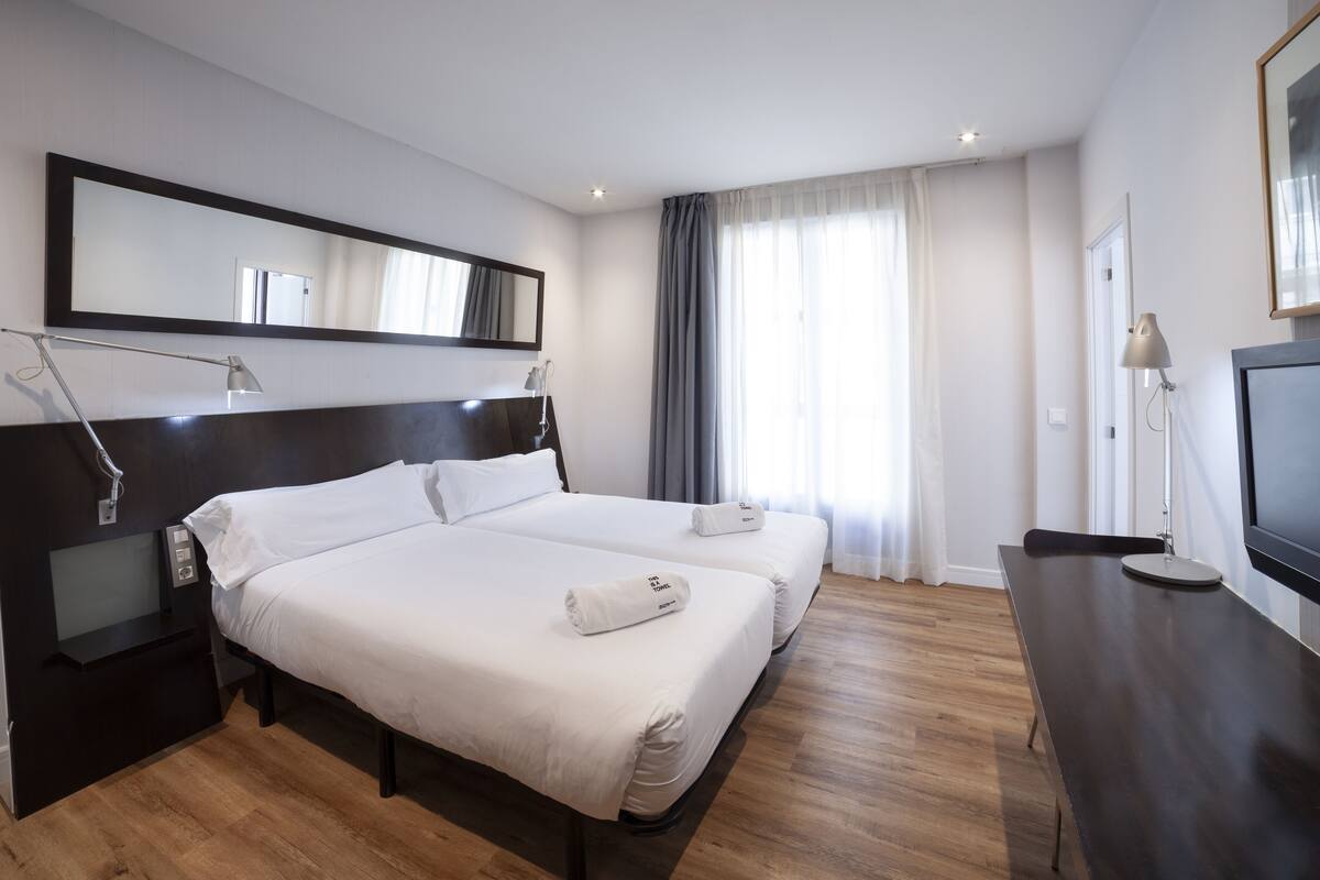 A hotel room with a large bed, bedside tables, a TV, and a mirror.