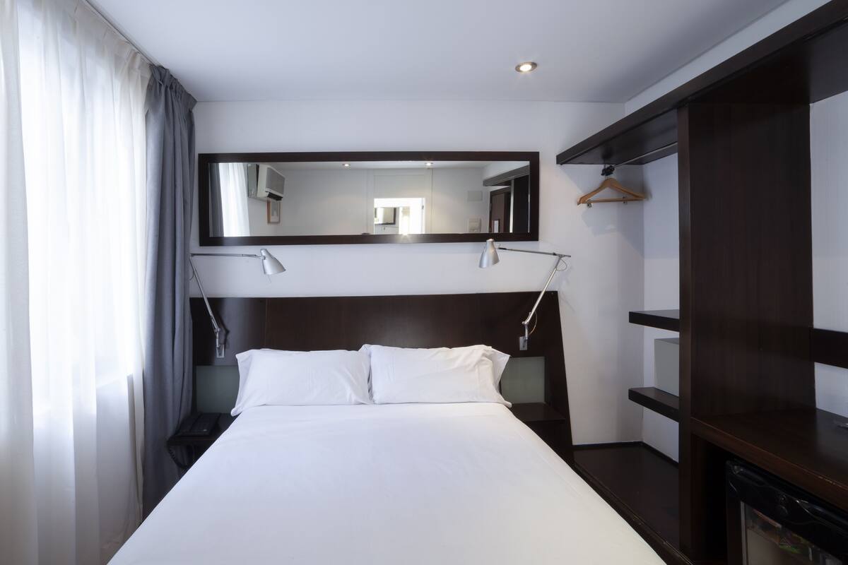 A hotel room with a large bed, a nightstand, a mirror, and a wardrobe.