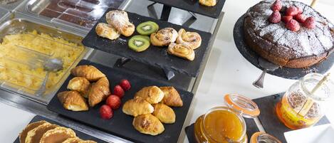 A buffet with various breakfast items including pancakes, pastries, and a cake.
