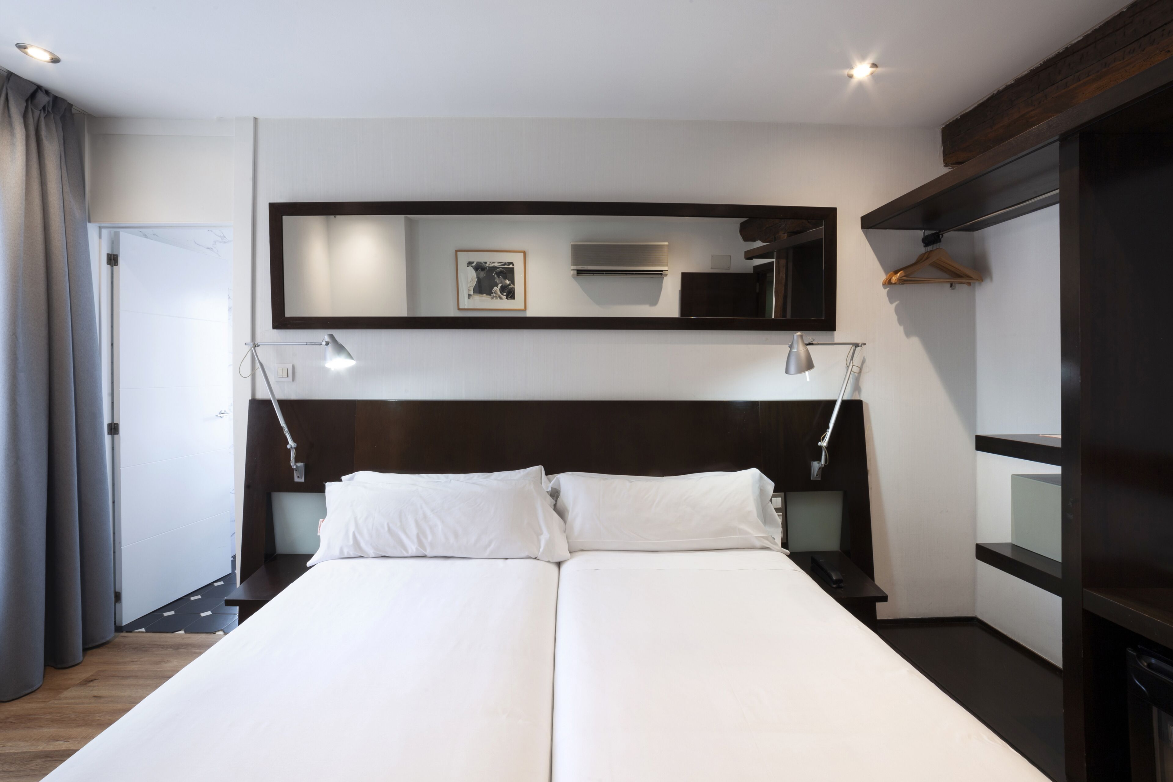 Una habitación de hotel moderna con una cama grande, lámparas de noche, un espejo y un armario.