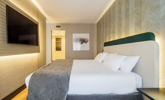 Habitación de hotel con cama, televisor de pantalla plana montado en la pared, estante empotrado y un cuadro en la pared.