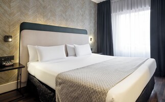 Ein Hotelzimmer mit einem großen Bett, einem Nachttisch mit Telefon und einer Wandleuchte.