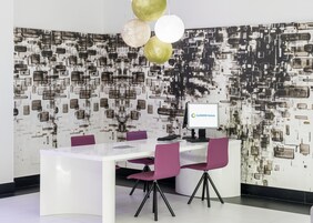 Una moderna area reception di un hotel, con una scrivania bianca, sedie viola e una parete decorata.