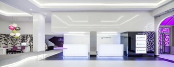 Ein moderner Hotel-Empfangsbereich mit minimalistischem Design, der einen Empfangstresen, ein digitales Display und ein an der Wand befestigtes Schild für ILINION Hotels zeigt.