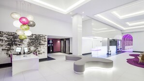 A modern reception area with a white reception desk, purple chairs, and a purple carpet. - Hotel ILUNION Suites Madrid (Madrid)
