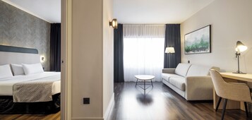 Ein Hotelzimmer mit einem Bett, einem Schreibtisch, einem Sessel, einem kleinen Tisch und einem Bild an der Wand.