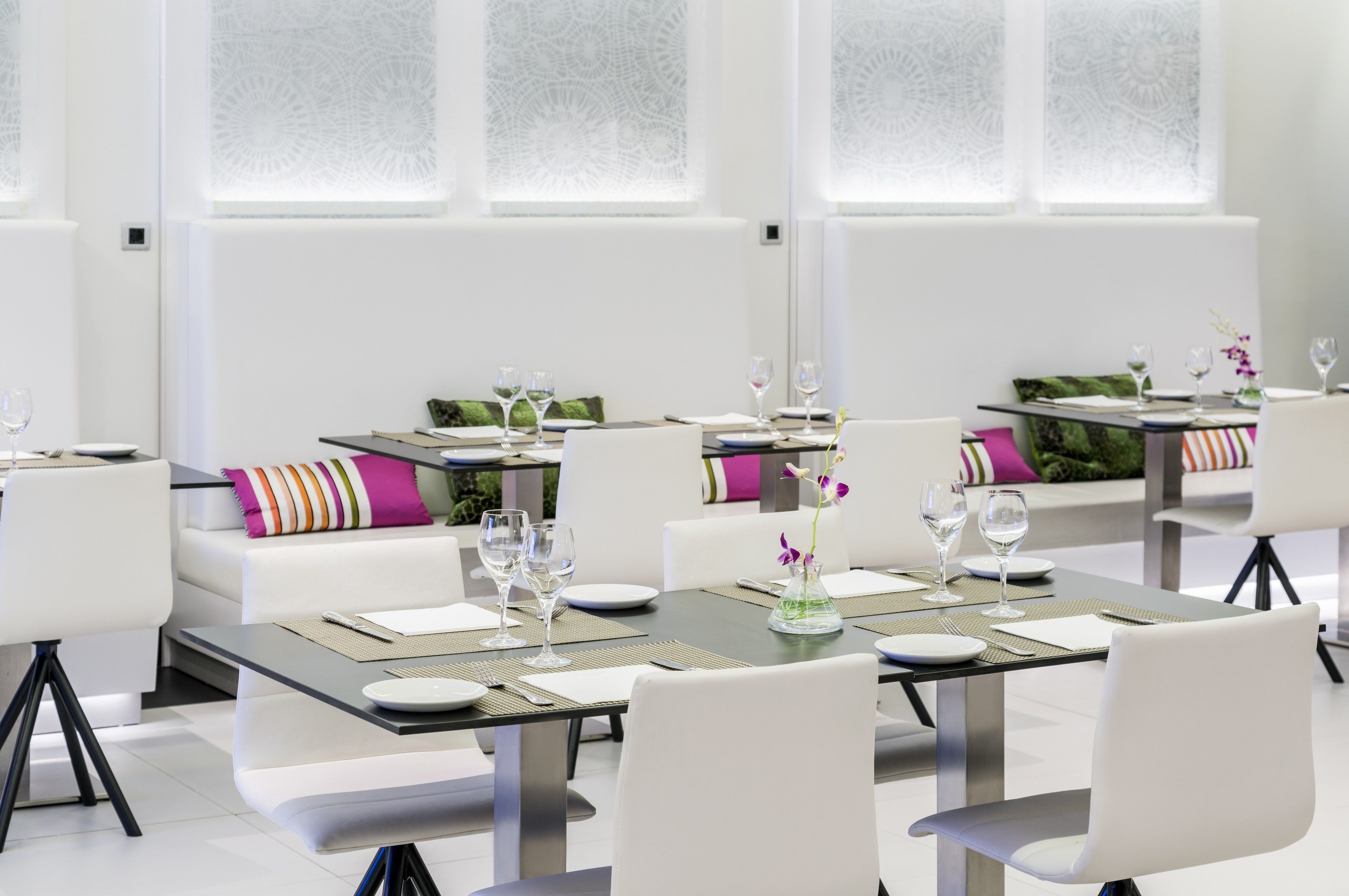 A modern dining area with tables set for two, white chairs, and a green vase with flowers.