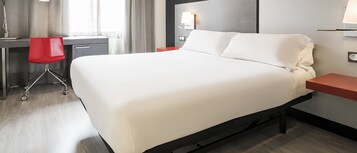 Una camera d'albergo con un letto grande, una scrivania con una sedia e un comodino con una lampada.