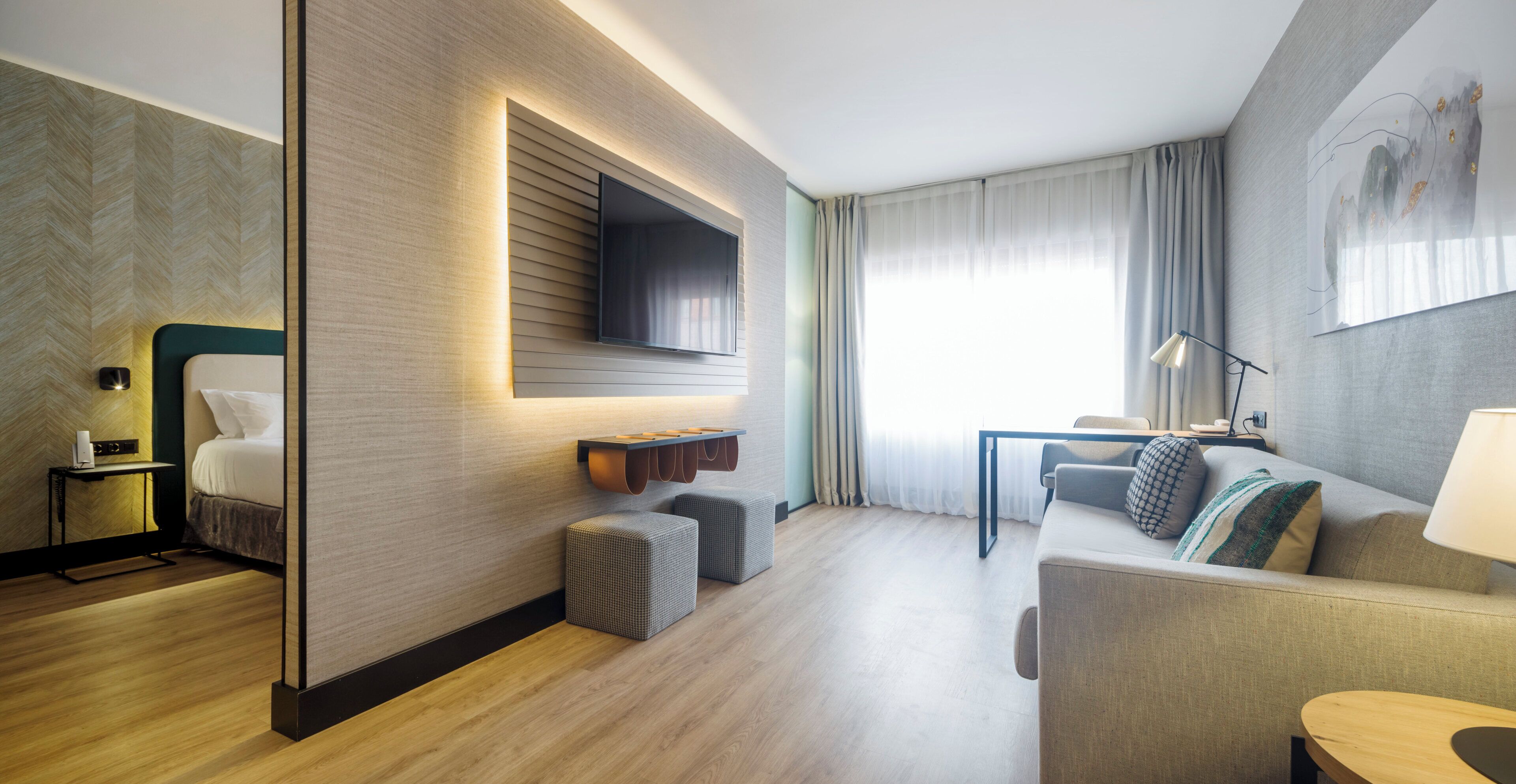Una habitación de hotel moderna con una televisión de pantalla plana montada en la pared, un sofá, una mesita y una lámpara.