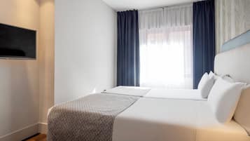 Una habitación de hotel con una cama, un televisor montado en la pared y una ventana con cortinas.