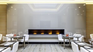 A modern dining area with a central fireplace, white chairs, and tables set for dining. - Hotel ILUNION Suites Madrid (Madrid)