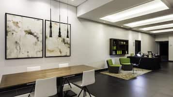 Una sala de conferencias moderna con una mesa larga, sillas blancas, arte abstracto en la pared y un sofá negro con cojines verdes.