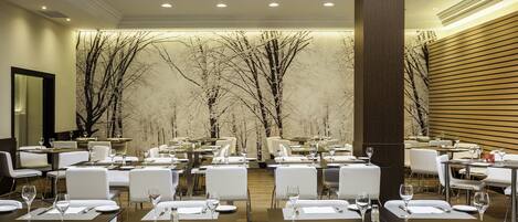 Un restaurante con varias mesas preparadas para comer, con una decoración moderna y un gran mural de un árbol en la pared.