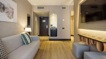 Una habitación de hotel moderna con sofá, una mesita, lámpara, mini refrigerador y televisión.
