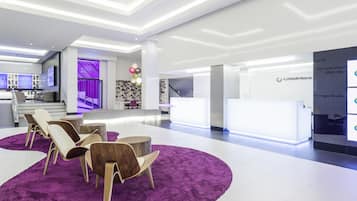 Un moderno vestíbulo de hotel con una recepción, una zona de estar con sillas y una alfombra morada.