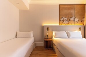 Una habitación de hotel con dos camas individuales, una mesita de noche con lámpara y un panel decorativo sobre la cama.