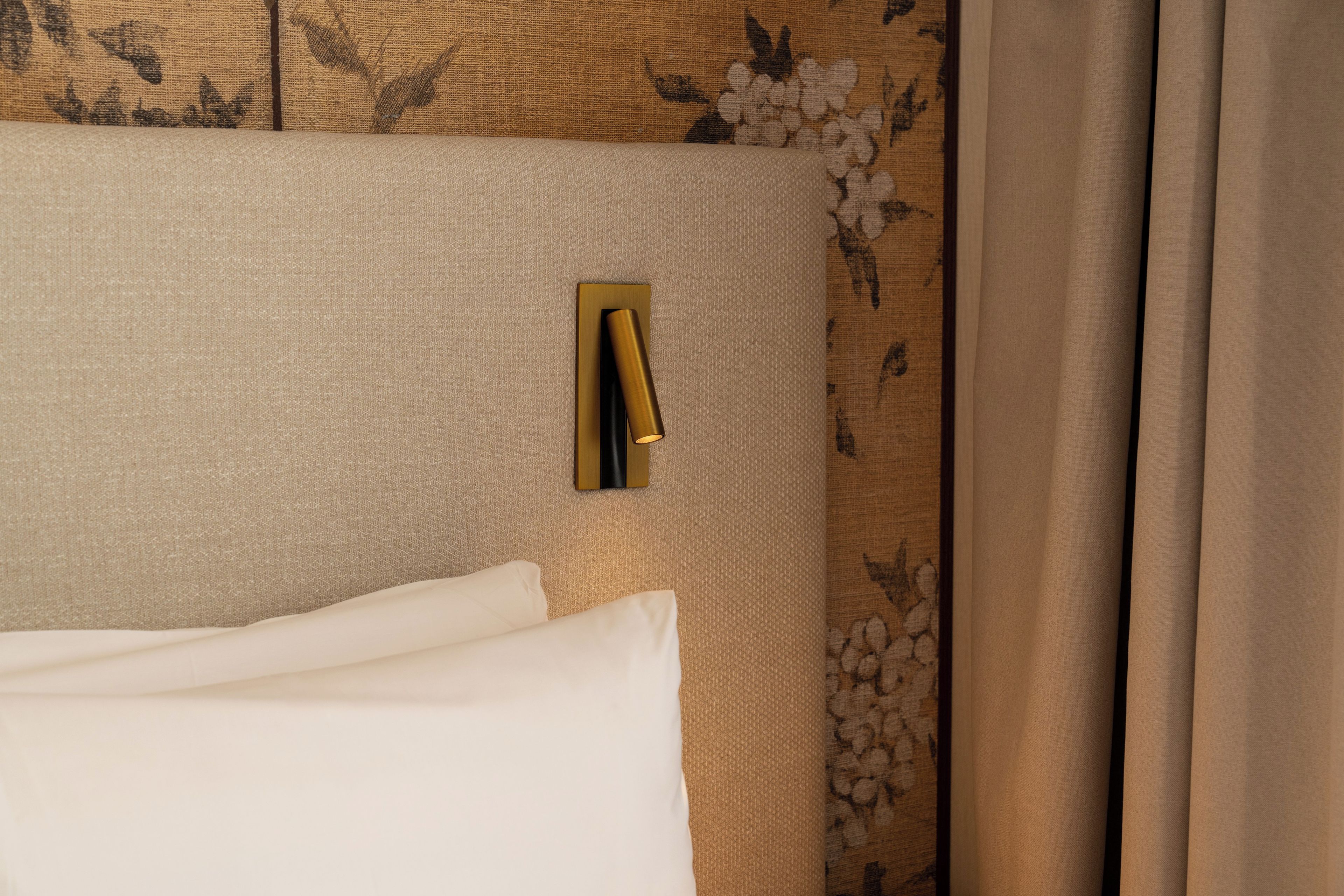 Una cama con cabecera texturizada, almohada blanca y lámpara de pared.