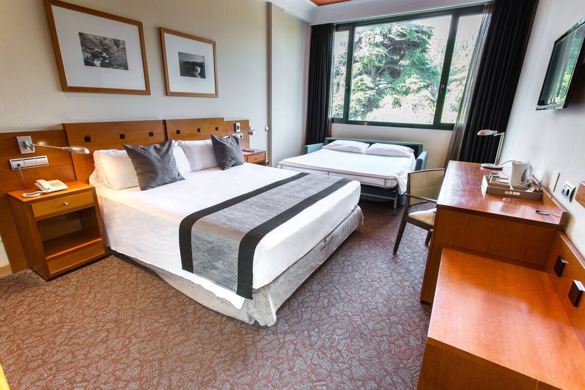 Hotelkamer met twee bedden, een bureau, een stoel, een nachtkastje, een lamp, een telefoon en lijstjes met foto's aan de muur.