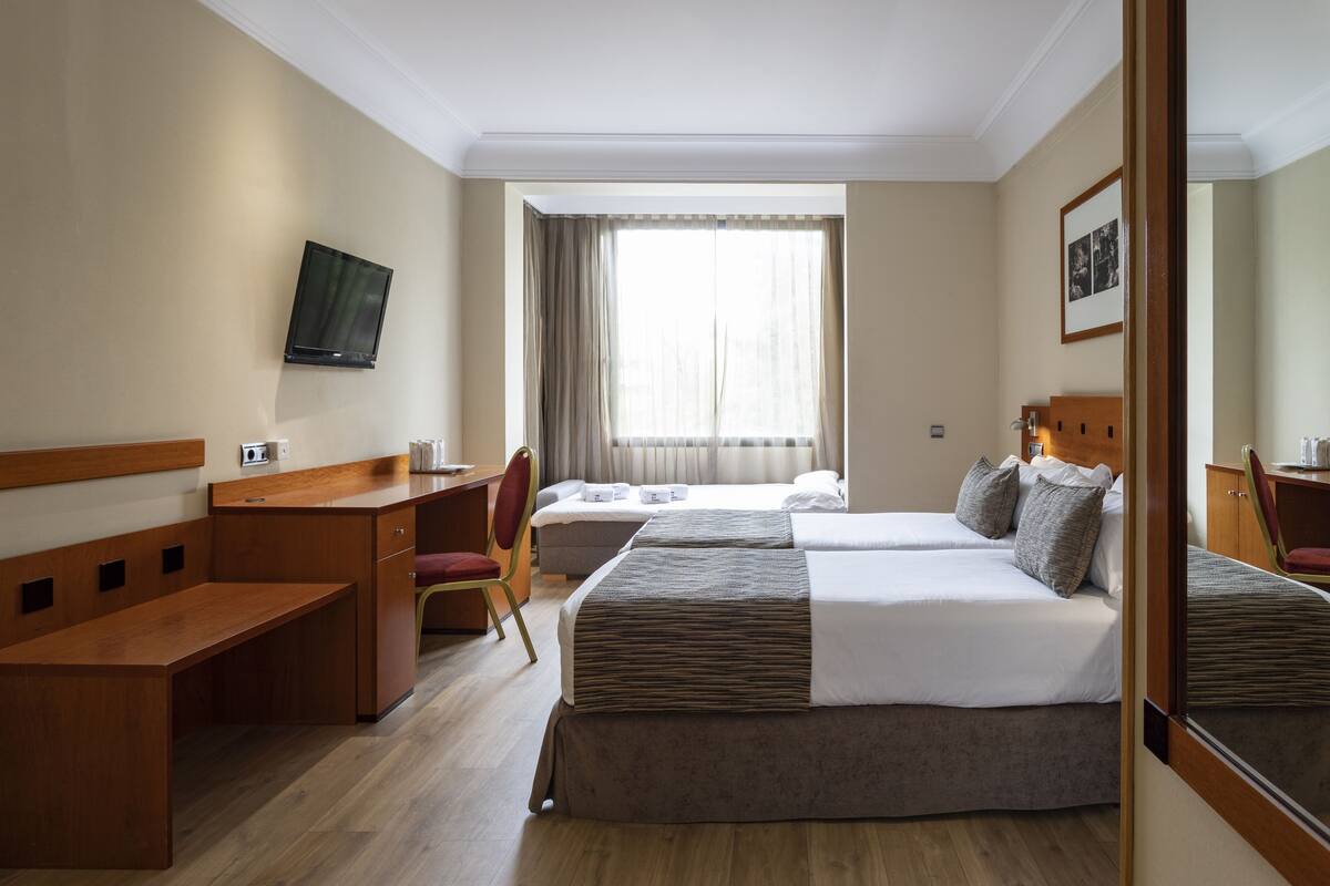 Een hotelkamer met een bed, bureau, stoel, televisie en raam met gordijnen.