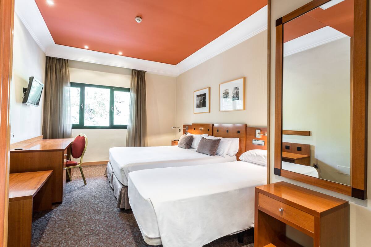 Een hotelkamer met twee bedden, een bureau, een stoel, een dressoir en een grote spiegel.