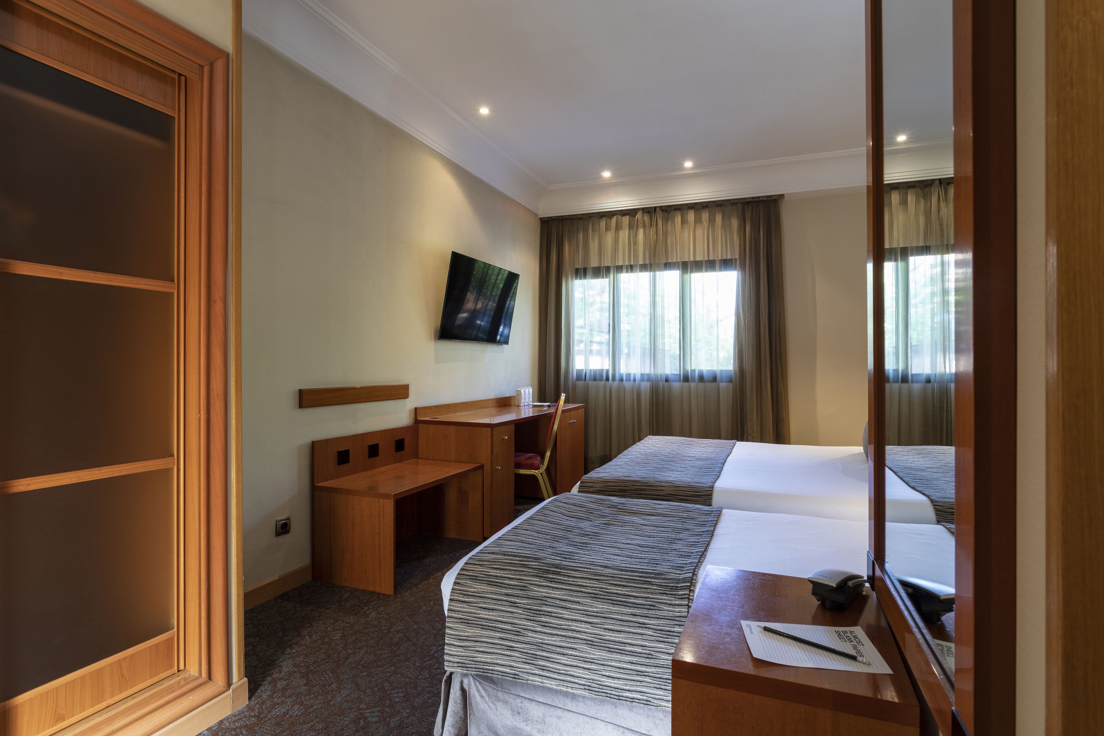 Une chambre d’hôtel équipée d’un lit, d’un bureau, d’une chaise, d’une télévision et d’une fenêtre avec des rideaux.