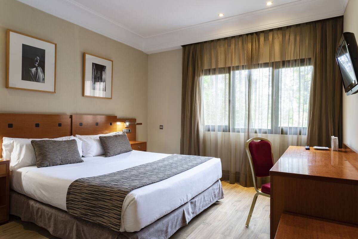 Een hotelkamer met een groot bed, een bureau, een stoel en twee ingelijste foto's aan de muur.