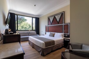 Ein Hotelzimmer mit einem großen Bett, einem Schreibtisch, einem Stuhl, einem Nachttisch und einem Fenster mit Vorhängen.