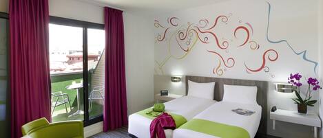 A hotel room with two beds, a desk with a laptop, a chair, a balcony with a table and chairs, and a decorative wall.