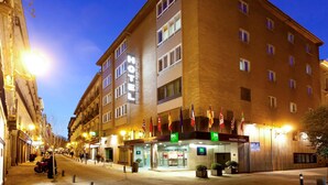 Egy többemeletes szálloda, feltűnő „HOTEL” felirattal és a bejárat felett elhelyezett zászlókkal.