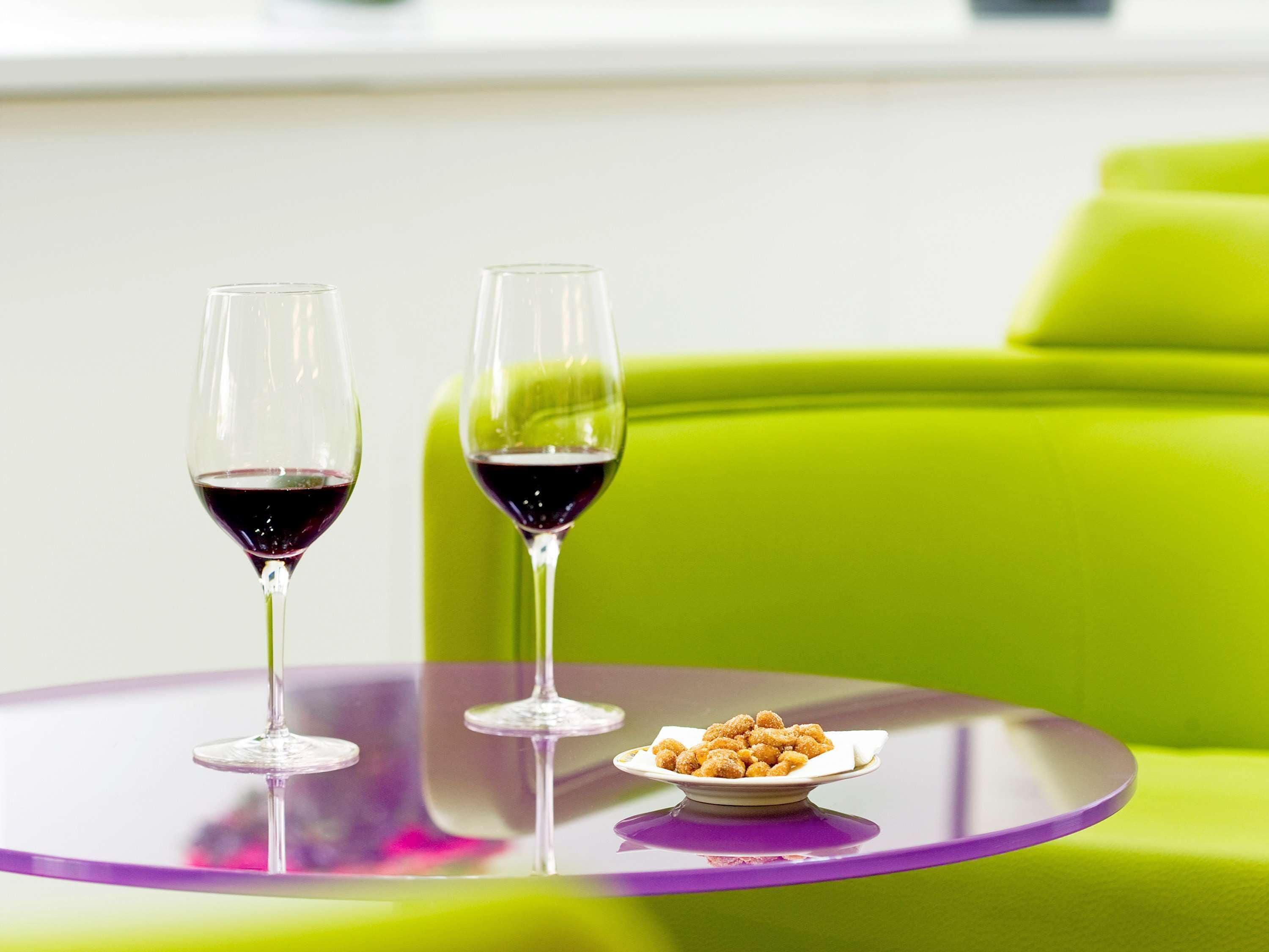 Dos copas de vino sobre una mesa morada con un cuenco de nueces a un lado, frente a un sofá verde.