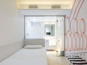 Ein modernes Hotelzimmer mit Bett, Duschkabine aus Glas, Waschbecken und einer Wand mit abstrakter Kunst.