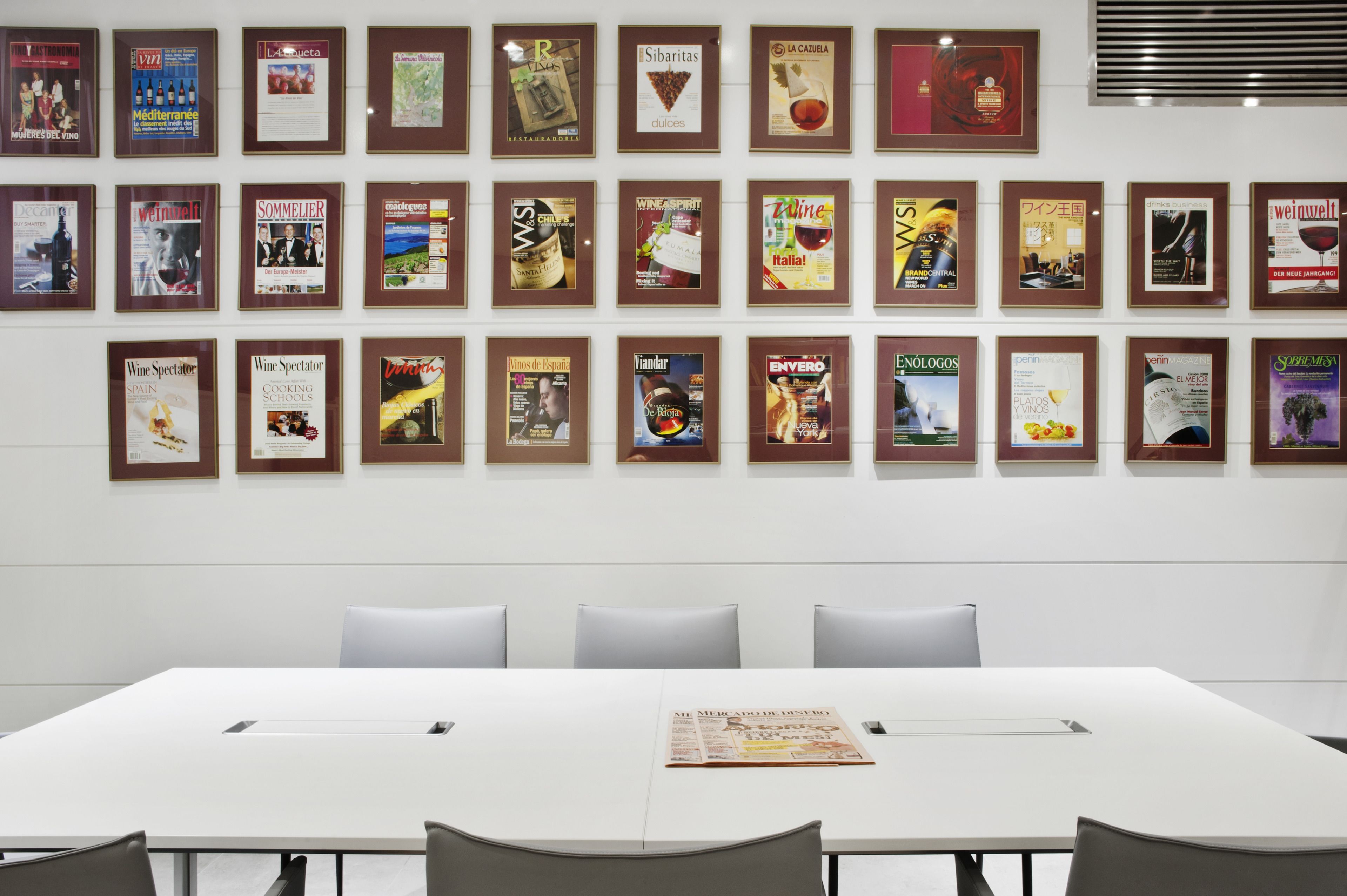 A conference room with a long table and several chairs, framed magazines on the wall, and a newspaper on the table.
