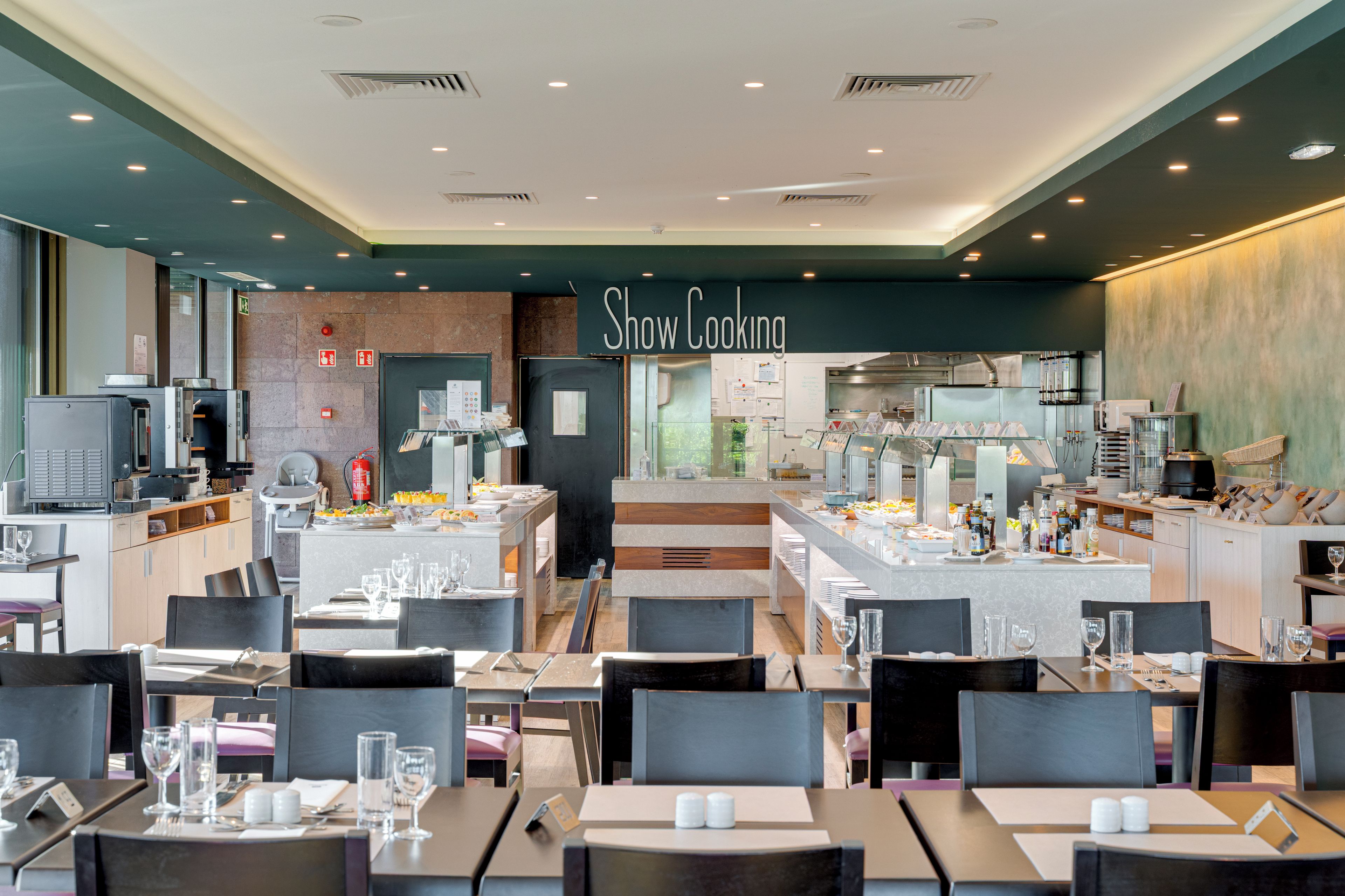 Un restaurant avec une enseigne indiquant « cuisine en direct », plusieurs tables et un espace cuisine.