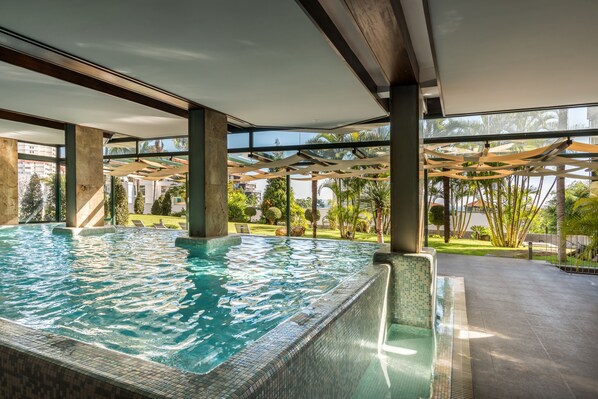 Una piscina techada, una piscina al aire libre, sombrillas