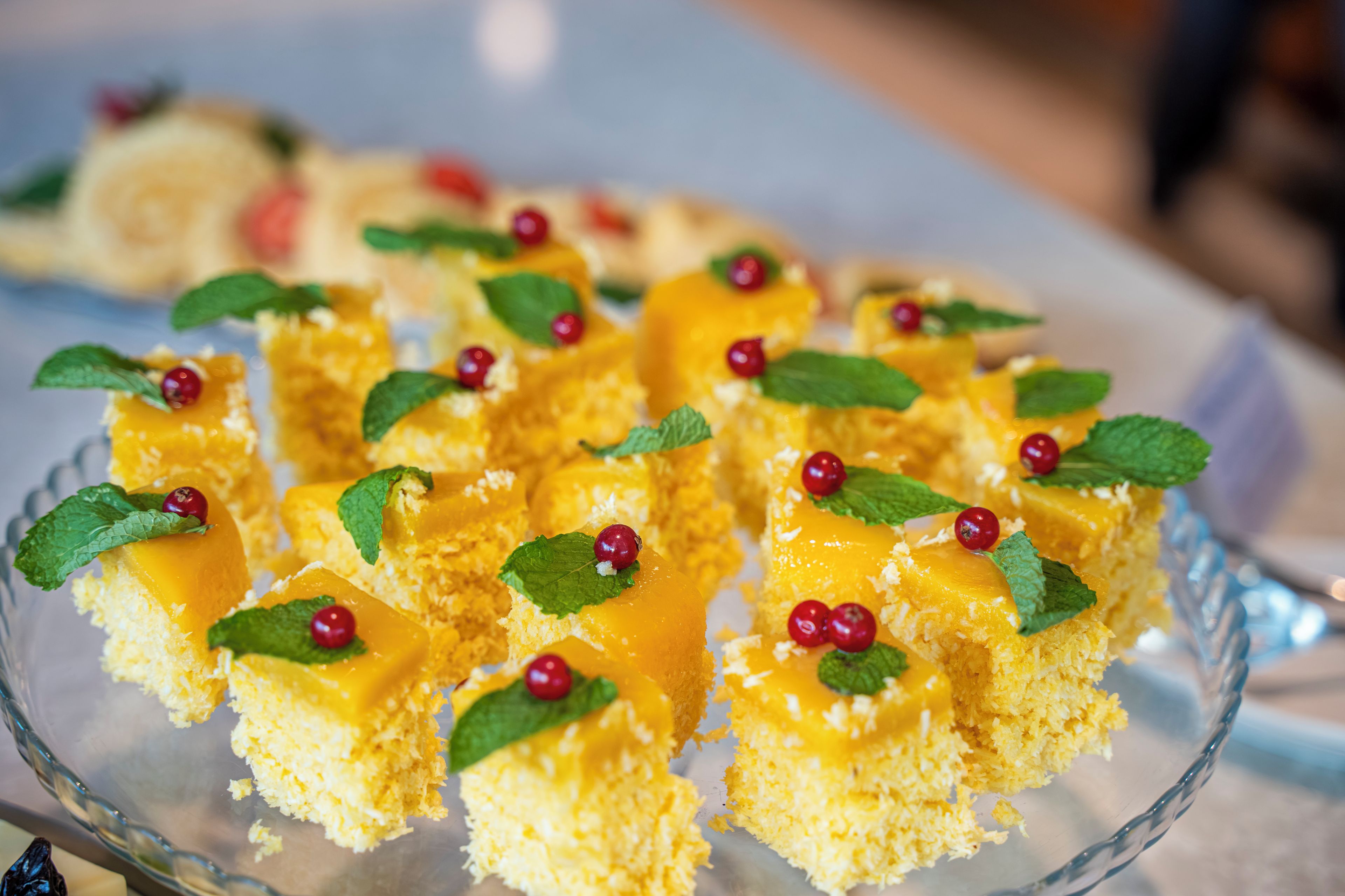 Een glazen bord met vierkante desserts, gegarneerd met muntblaadjes en rode bessen.