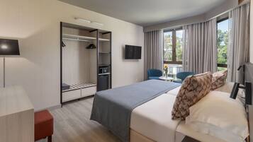 Une chambre d’hôtel moderne dotée d’un grand lit, d’un bureau, d’une armoire, d’une télévision et d’un balcon avec des rideaux.