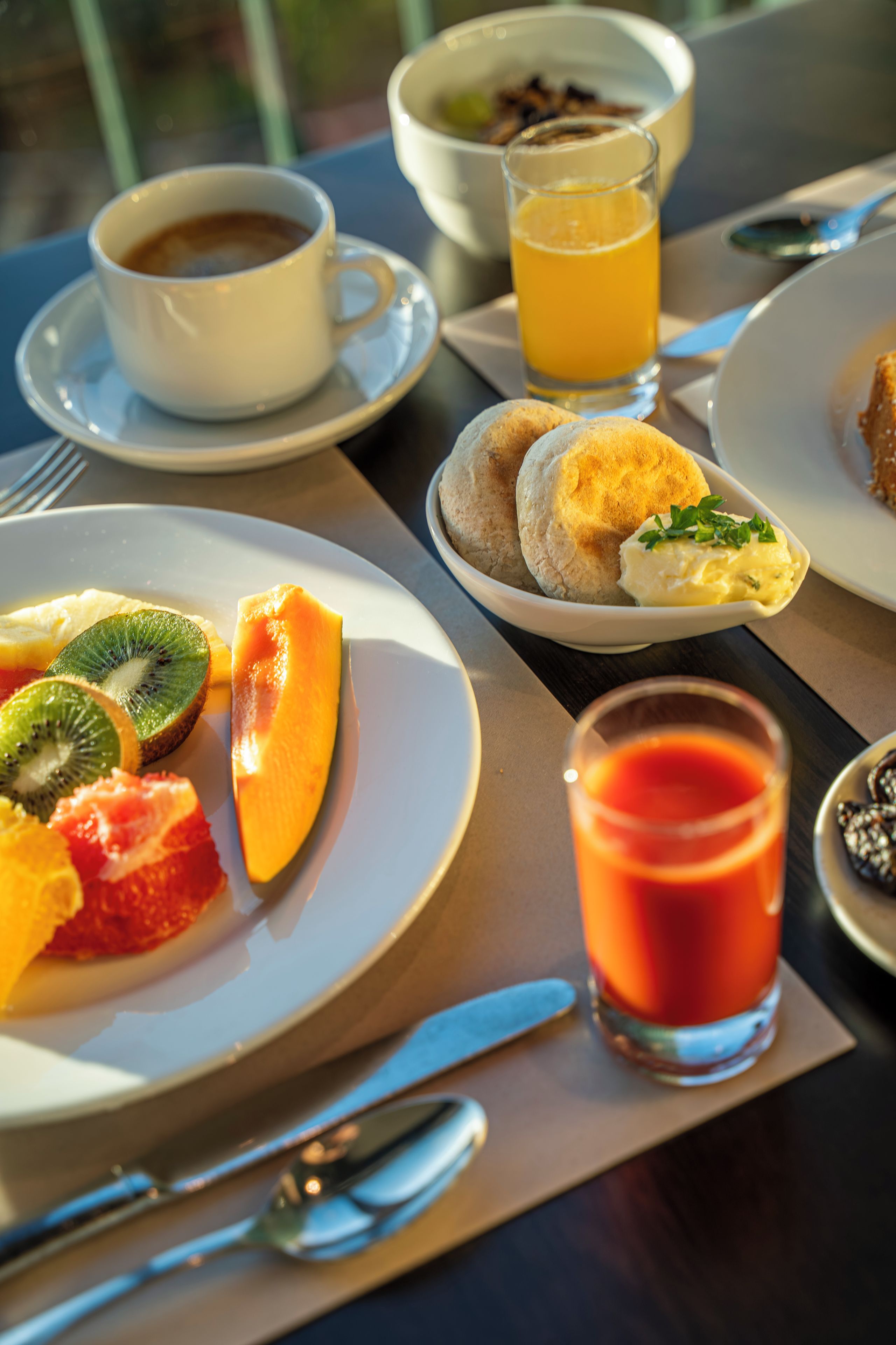 A breakfast setting with plates of fruit, a glass of orange juice, and a cup of coffee.