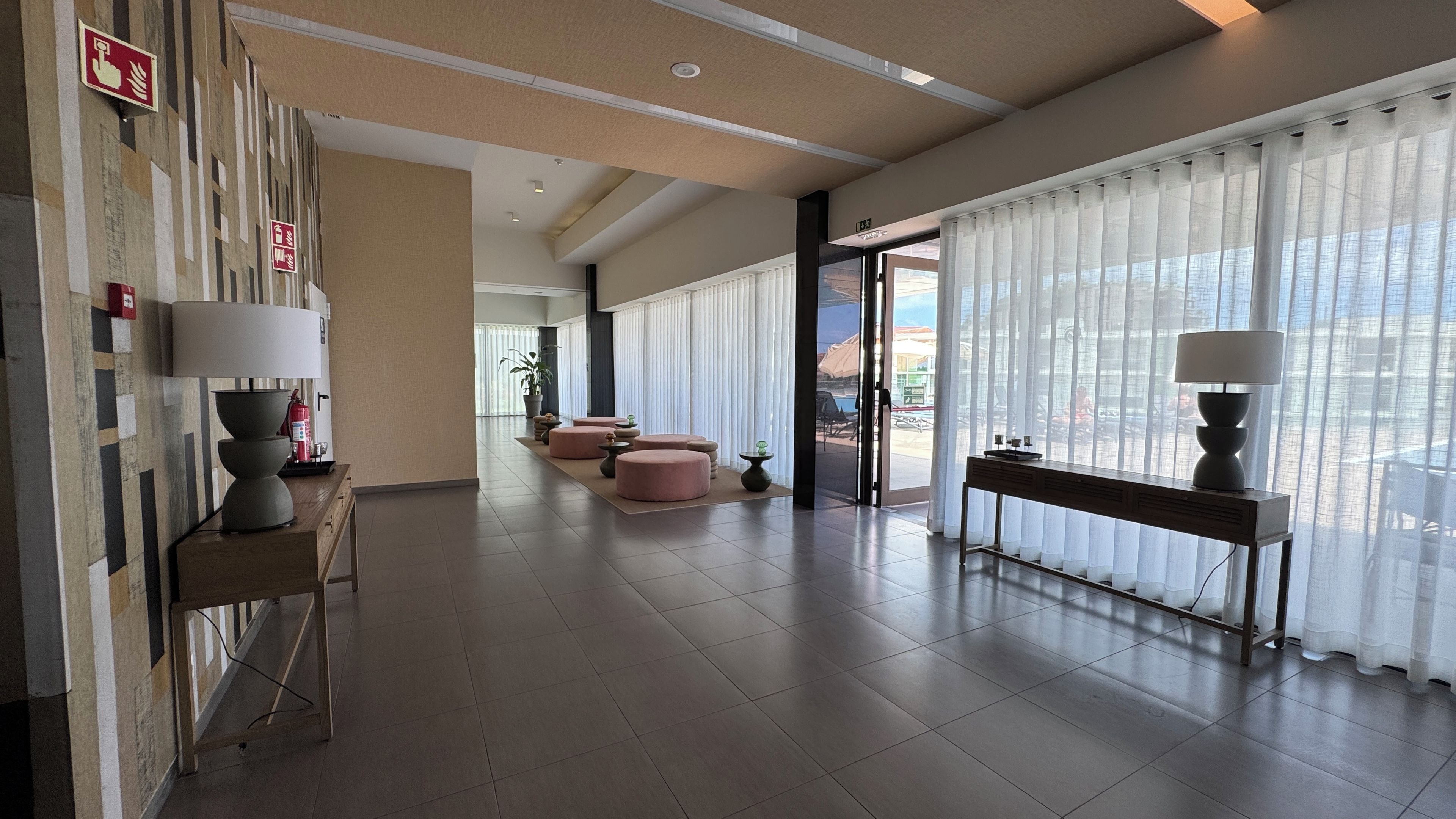 Una hall d'albergo con reception, area relax e ampie finestre con tende leggere.