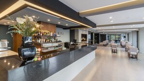 Uma área de bar moderna com um balcão comprido, banquetas e um vaso decorativo com flores.