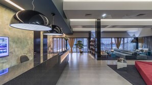 Um lobby moderno com balcão de atendimento, área de estar e grandes janelas com vista para a cidade.