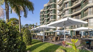 Pátio de hotel com área de estar ao ar livre, palmeiras e um edifício com vários andares e varandas.
